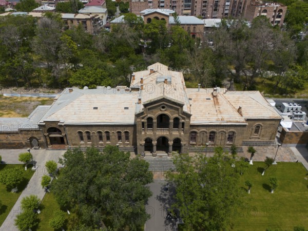 Historic building with classical façade surrounded by lush vegetation and urban area, aerial view,