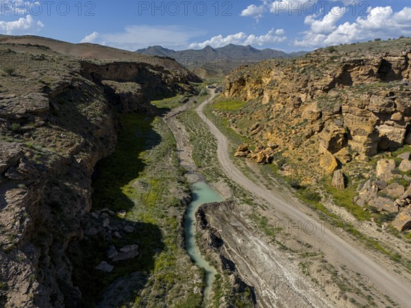 Long valley with narrow river, flanked by steep cliffs, under blue sky with some clouds, aerial