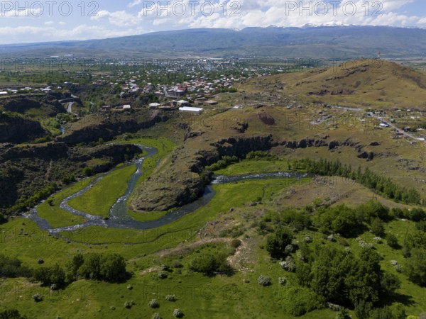 River flowing through a hilly landscape with a city in the background under a blue sky, aerial