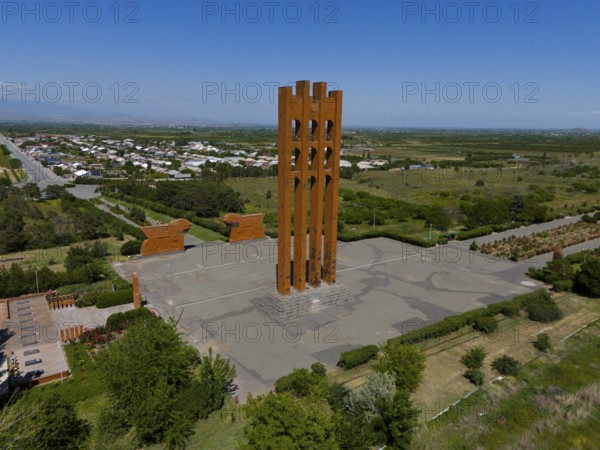Large modern monument surrounded by landscape and small buildings under blue sky, aerial view,