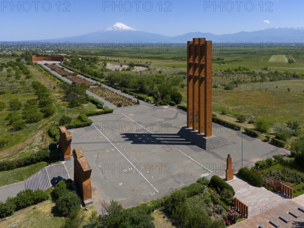 Large modern monument in front of a mountain panorama under a clear blue sky, aerial view,