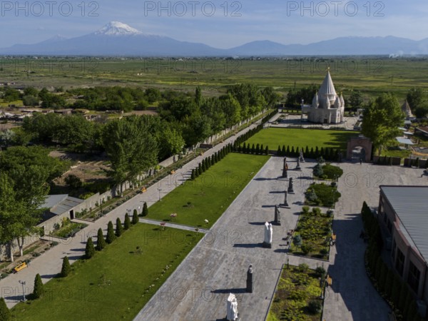 Spacious garden with statues and temple, surrounded by nature and mountains in the distance, aerial
