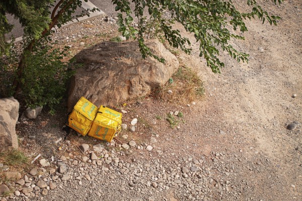 08/25/2025 Georgia, Tbilisi, Delivery packages, Glovo company, left on stony ground, near bushes,