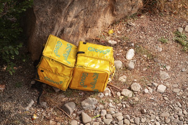 08/25/2025 Georgia, Tbilisi, Delivery packages, Glovo company, left on stony ground, near bushes,