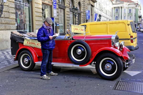 Prague, Czech Republic, Europe, Man reading in front of a classic red vintage car on a busy street