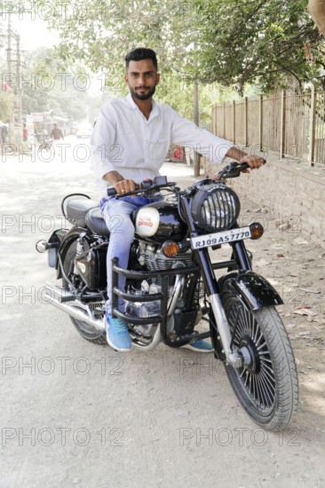 Kota, Rajasthan, North India, Asia, Man sitting on a black Royal Enfield motorbike on a dusty road,