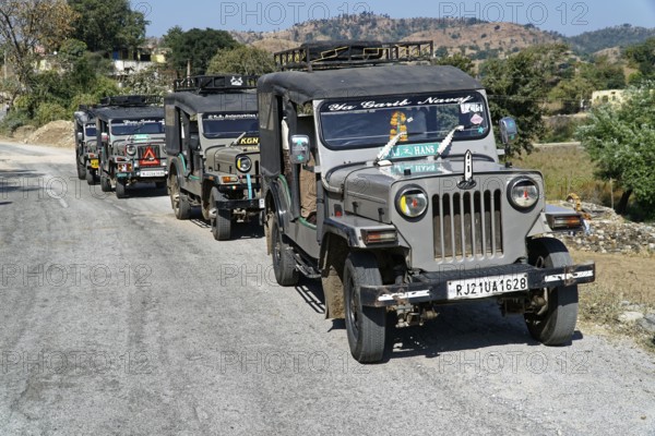A convoy of jeeps drives along a country road in a mountainous region, Ranakpur, Jodhpur,