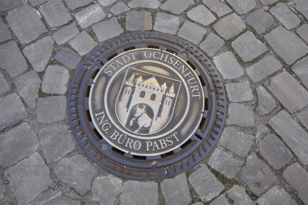 Round manhole cover with town coat of arms and inscription, paving stones, ground, Ochsenfurt,