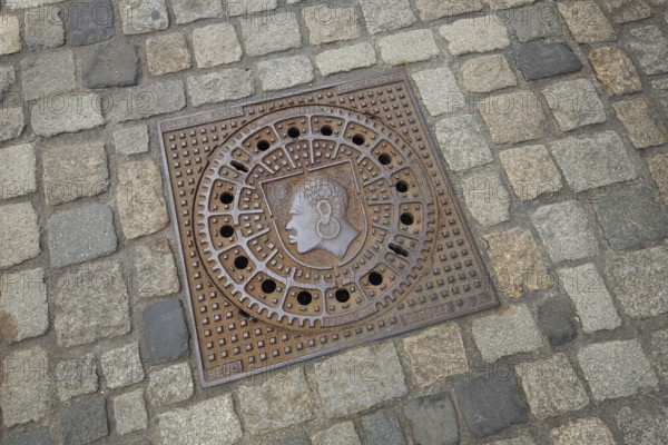 Square manhole cover with city coat of arms, inscription, paving stones, floor, African head with