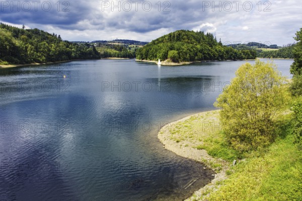 A lake (Aggertalsperre) with a wooded island and trees on the shore under a summer sky,