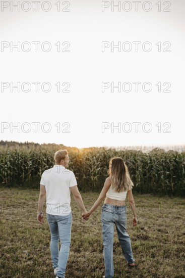 Couple walking hand in hand across a mown field