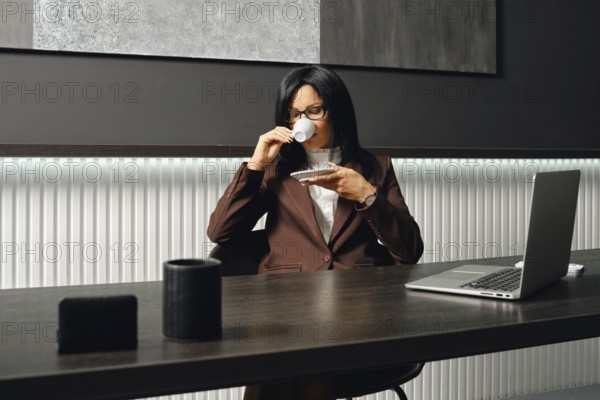 A real estate agent in a brown suit sits at a desk, sipping coffee from a small cup in a