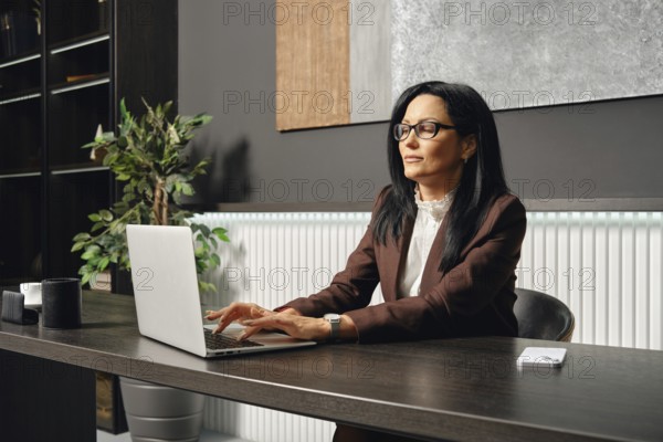 A businesswoman sits at a desk and typing on her laptop in an office. The space features elegant
