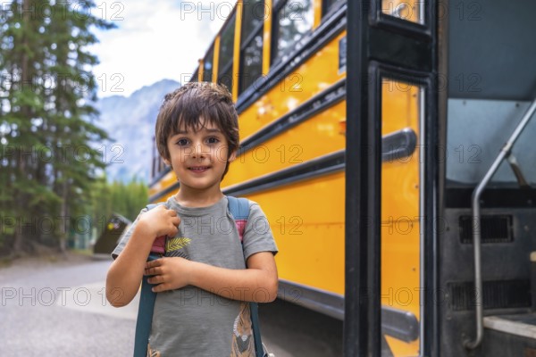 Happy elementary school student carrying backpack is waiting for the school bus in a mountain