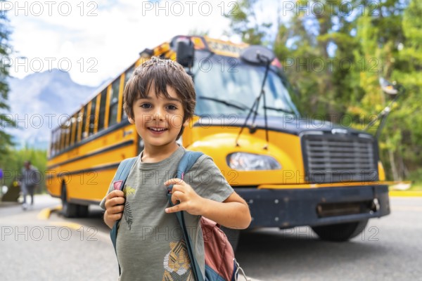 Happy schoolboy carrying backpack is waiting for the school bus in front of blurred mountain