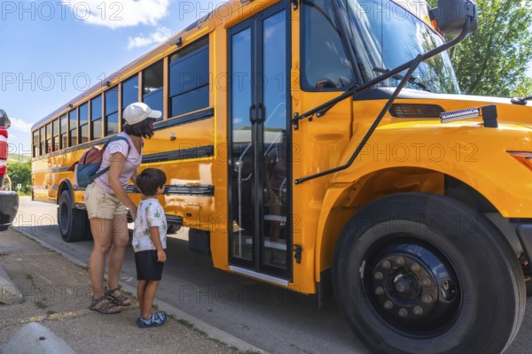 Caring mother supports her son as he prepares to board the school bus for his first day back to