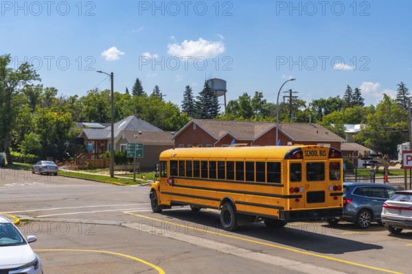 Classic yellow school bus driving away from an intersection in a quiet residential area, marking