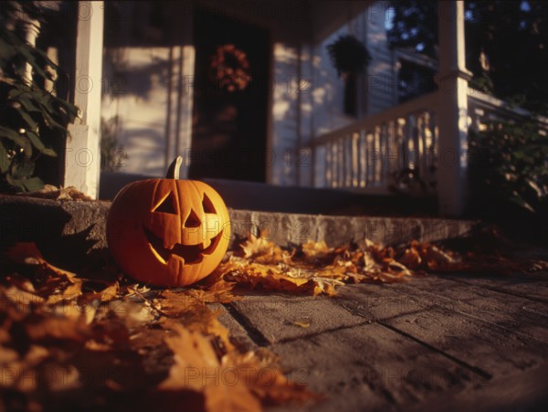 A carved pumpkin with a smiling face stands on a house wall in front of a residential building,