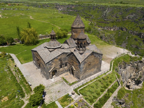 Medieval stone church with a surrounding green landscape and cliffs, aerial view, Saghmosavank