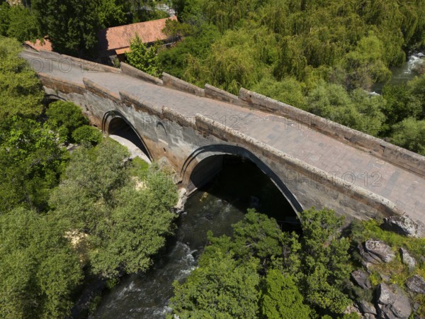 Stone bridge with arches over a river, surrounded by lush trees and nature, aerial view, Three-arch