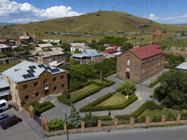 Aerial view of a village with a church and a hill in the background under a blue sky, aerial view,