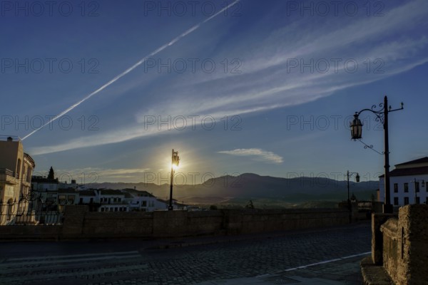 Sun rising behind mountains, illuminating street lamps on cobblestone bridge at dawn in ronda,