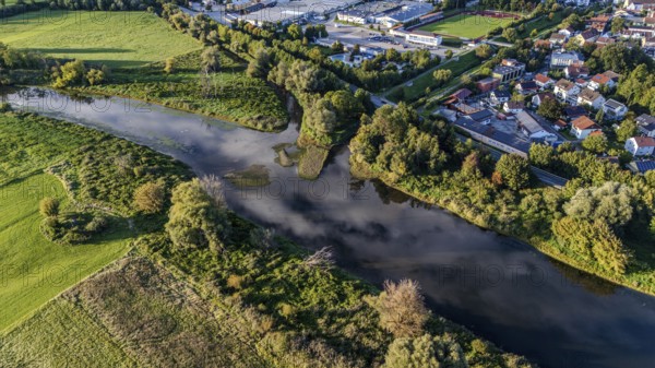 An idyllic landscape shows a gently flowing river, surrounded by lush vegetation and a small town
