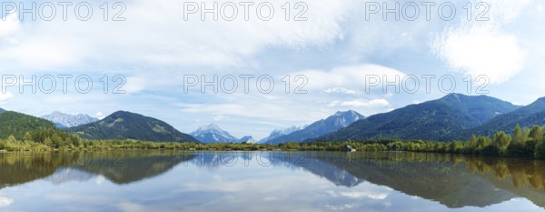 Panoramic lake reflects the surrounding mountains and the slightly cloudy sky, Admont, Styria,