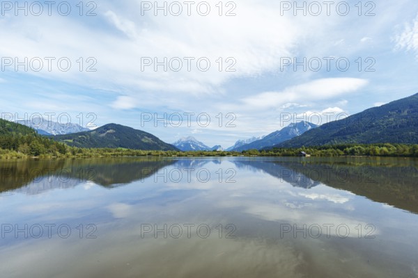 Panoramic lake reflects the surrounding mountains and the slightly cloudy sky, Admont, Styria,