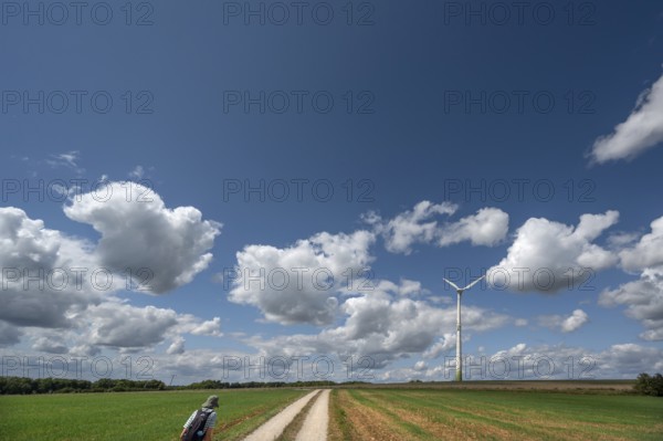 Hiker on a country lane in Franconian landscape, a windmill behind, cloudy sky, Karsberg, Upper