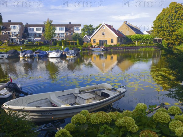 Boats on a quiet canal with reflection of houses in the water, surrounded by green landscape,