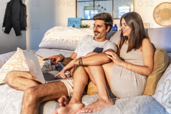 Young couple relaxing on comfortable sofa, browsing internet on laptop, enjoying time together in