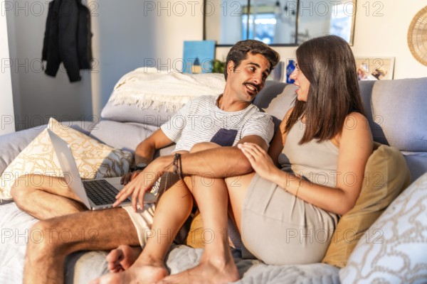 Young couple relaxing together on a comfortable sofa at home, browsing internet on a laptop and