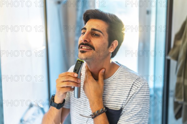 Man trimming his beard using an electric razor, taking care of his appearance in the bathroom