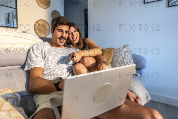 Young couple enjoying a movie on their laptop, laughing and having a good time together on the sofa