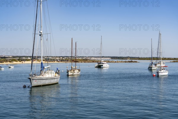 Sailboats anchored in the Gilão River, in front of the beach Praia da Ilha de Tavira, on the island