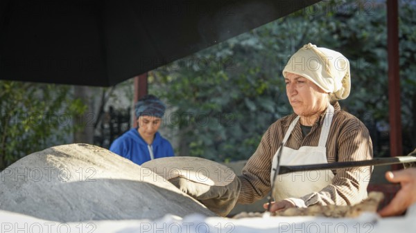 A Turkish woman bakes traditional bread on a clay tandoor oven in a rural village, Hatay, Hatay,