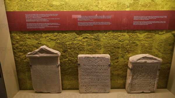 Three ancient Hebrew tombstones in an exhibition with yellow background, Kahal Shalom Synagogue,