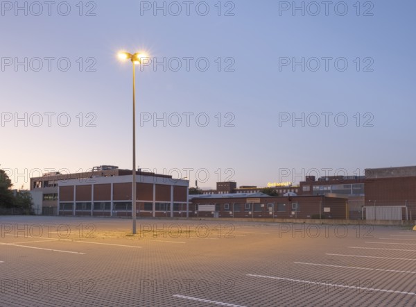 Taking a street lamp on an empty car park in front of an industrial building in the evening,