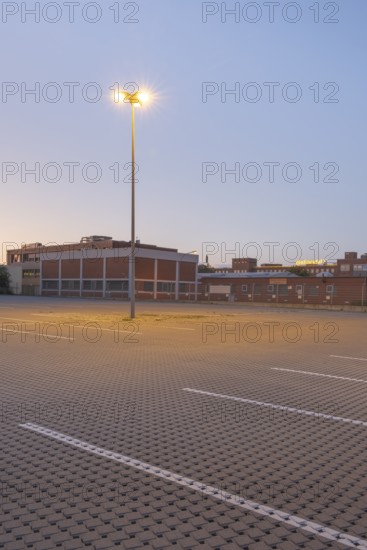 Taking a street lamp on an empty car park in front of an industrial building in the evening,