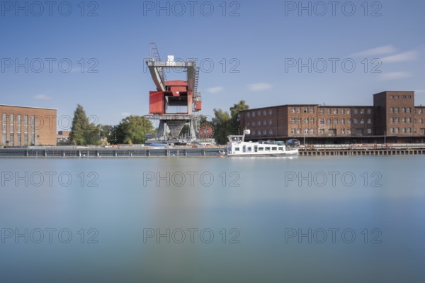 View over the Mittelland Canal to an industrial building and a crane in front of a ship, long