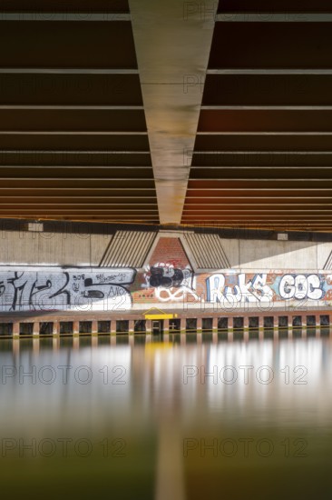 View across the Mittelland Canal to the underside and the graffiti-painted abutment of a bridge on
