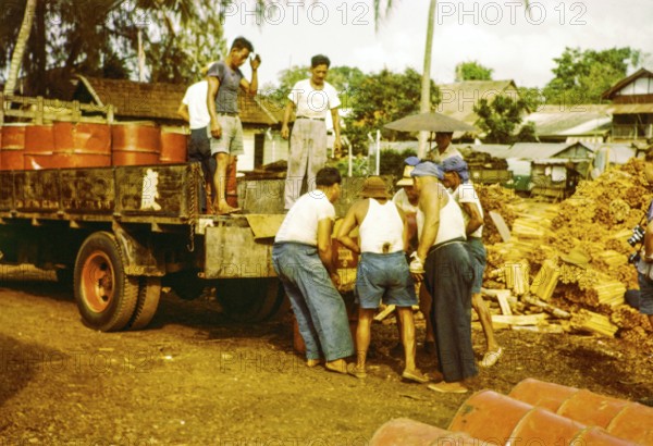 Male workers loading metal fuel drums onto back of lorry in timber yard, Johor Bahru, Johor,