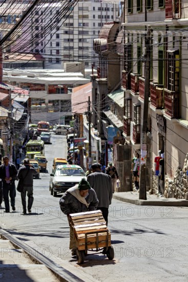 A man pushes a cart on a busy city street. Buildings and cars can be seen in the background, A man