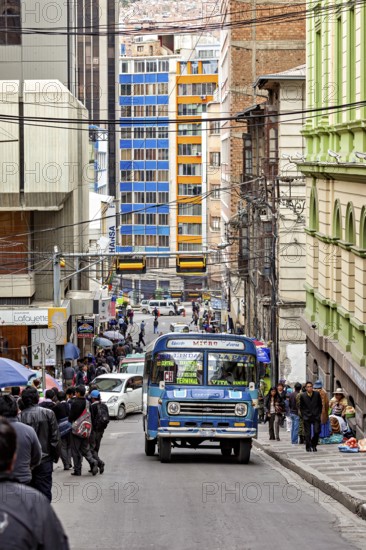 Busy city street with a blue bus and many people during the day in the middle of tall buildings, A