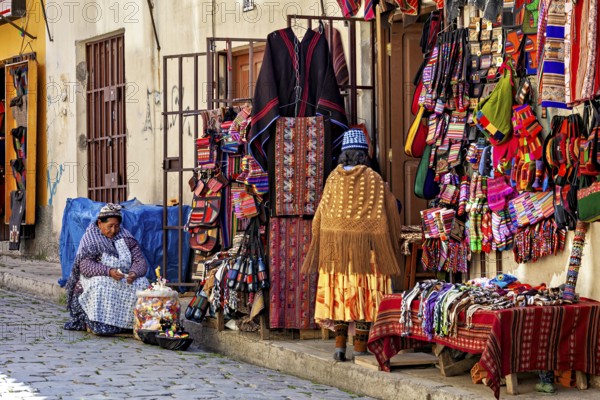 A woman sits in front of a market stall selling a variety of colourful textiles and traditional