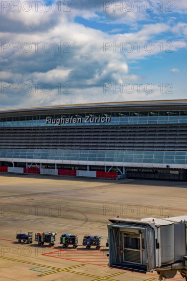 Zurich Airport and Building and Boarding Bridge Gate and Lugage on Trailer on Airfield in a Sunny