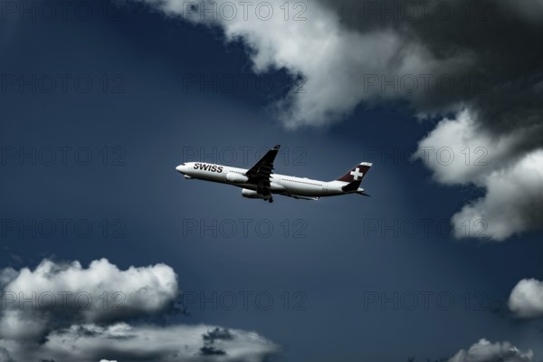 Swiss Airlines Passenger Airplane Flying Against Blue Sky and Clouds in a Sunny Summer Day From the