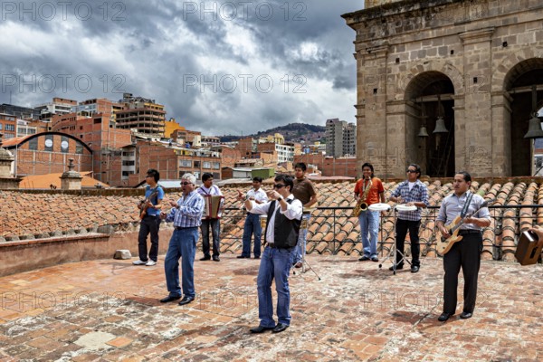 Group of musicians on a tiled roof in front of an urban backdrop with clouds in the sky, A music