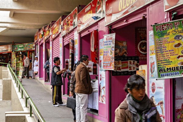 Row of pink market stalls with colourful signs, people ordering food, small shops and restaurants